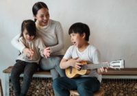Ethnic boy playing ukulele while sitting with mother and sister